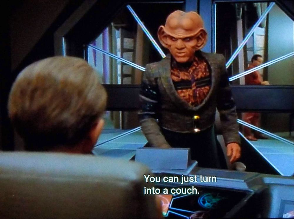 DS9 scene. Quark, a ferengi with a smooth large bald butt like head and big exaggerated earlobes is standing in Odo's office and speaking at him with an intense smoulder. We see Odo from behind in his chair. Closed caption reads, "You can just turn into a couch."