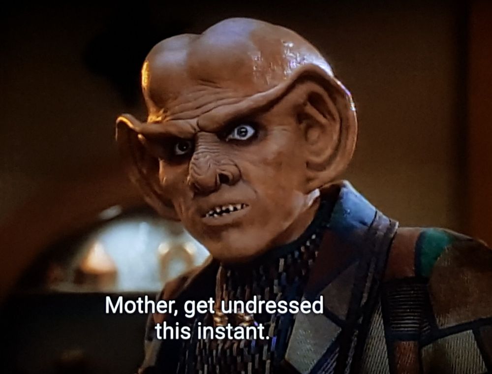 Star Trek Deep Space Nine scene. Quark is pictured up close. He's a Ferengi with sharp baby teeth and ginormous ear lobes and an exaggerated bald and bulbous head. He's wearing a jacket inspired by the set of the Arsenio Hall show. He looks serious but also shooketh. Closed caption reads, "Mother, get undressed this instant."
