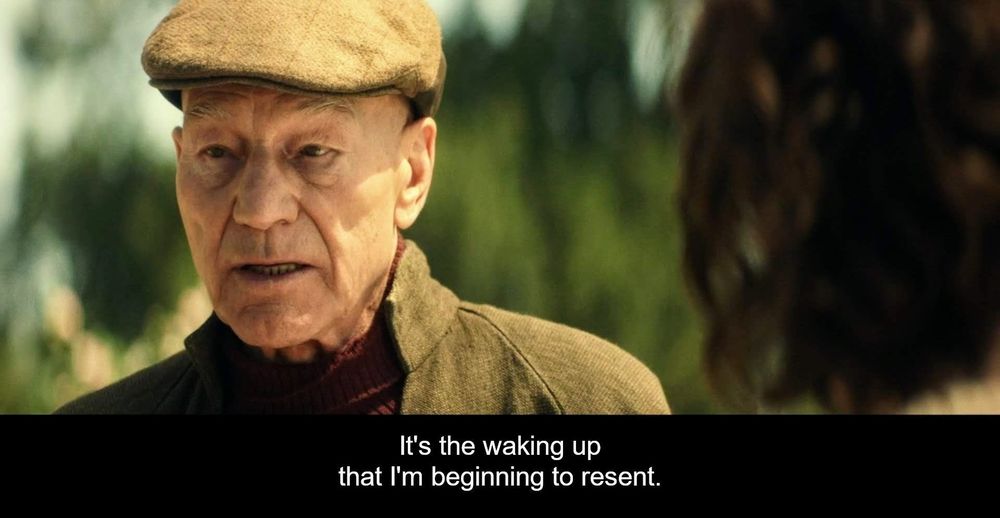 Star Trek Picard scene. An older civilian Picard is pictured outdoors with trees and he's talking to someone just off screen. He's dressed casually and looks nice. Not much else happenening on this one. Closed caption reads, "It's the waking up that I'm beginning to resent."