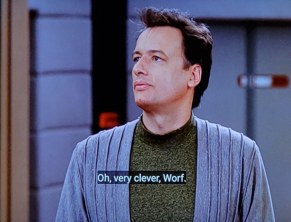 Star Trek The Next Generation scene. Q (an otherwise normal human looking guy) is standing on the bridge of the Enterprise D. He's wearing a grey robe and green undershirt. He's talking to someone off screen. (It's Worf)
Closed caption reads, "Oh, very clever, Worf. Eat any good books lately?"