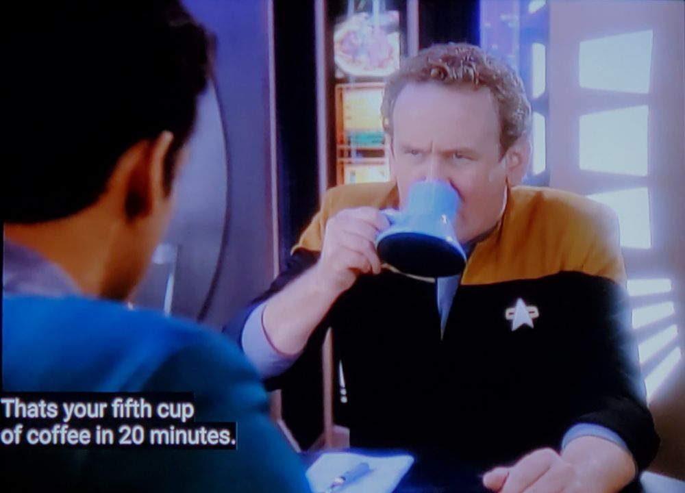 Star Trek Deep Space Nine scene. 
We're on a space station, number 9 I think. 
We're on the promenade and Dr Bashir is sitting and having a coffee chat with Chief Miles Edward O'Brien, who can perfectly fold a fitted sheet with one hand. O'Brien, who can beat you at tic tac toe in 2 moves, looks rather grumpy while taking a big swig of coffee from his future space coffee mug. Closed caption reads, "That's your fifth cup of coffee in 20 minutes."