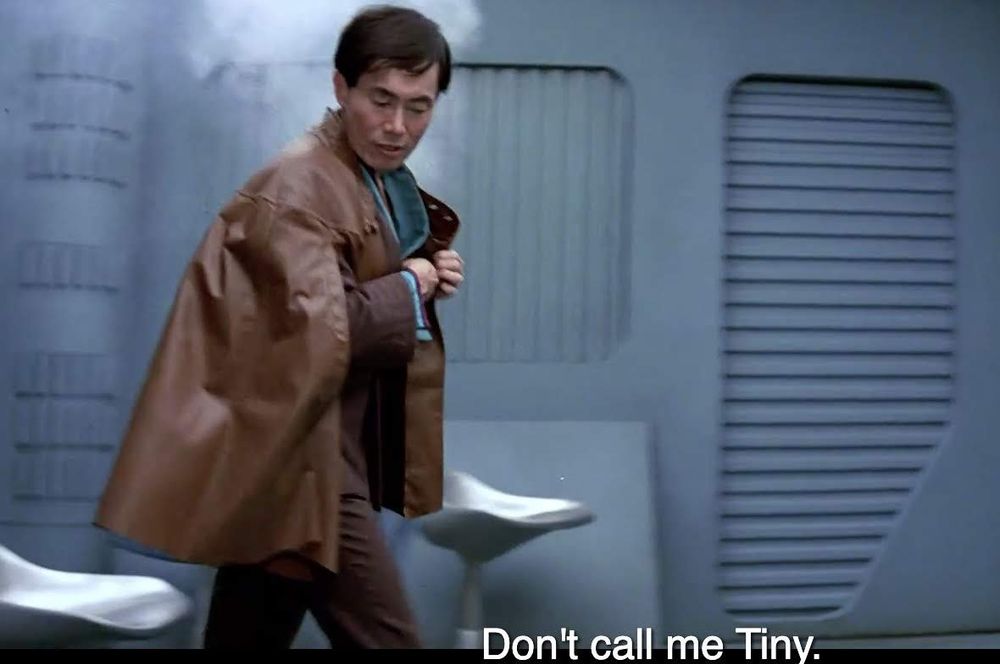 Star Trek The Search for Spock scene. We're in a future space room of some kind. Sulu is wearing a swaggy leather jacket that has cape features. He's walking and looking down at something as he passes it and there's a puff of smoke behind him. Closed caption reads, "Don't call me Tiny."