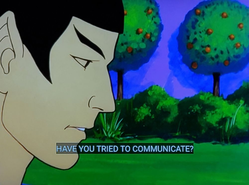 The Animated Series scene. Picture One is Spock up close in profile shot, with a lush green forest background. Closed caption reads, "Have you tried to communicate?" Picture 2 & 3 is a different Starfleet officer, gold uniform. He's standing in a Willy Wonka/Dr Suess looking scene with a structure behind of reds, yellows, greens, and blues, both in a wall and bench, with a similar colored structure beyond. Closed caption reads, "Yes sir. But all we've been able to arouse in them is a sort of quivering motion."