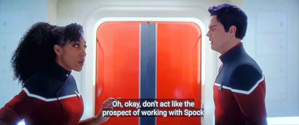 Star Trek Strange New Worlds scene kind of but also Star Trek Lower Decks scene but that's all I can say and if this confuses you just watch more Star trek. Anyhoo, we see a non-cartoon Bradward Boimler and Mariner standing in a corridor on the Strange New Worlds Enterprise outside a beautiful orange door and talking. Both are in Lower Decks era uniforms with red bottom/white crisp stripe across the chestal region and black shoulers. Boims looks distressed, as per usual. He also has slightly purple hair. Mariner is speaking, closed caption reads, "Oh, okay, don't act like the prospect of working with Spock doesn't tick off some weird box for you."