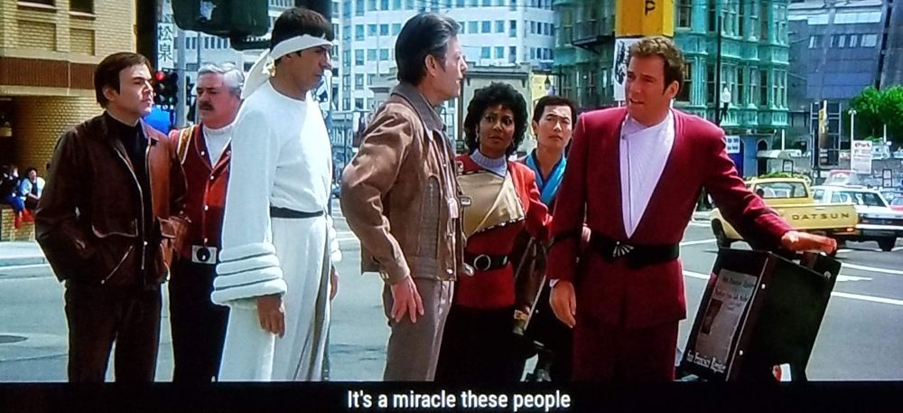 Star Trek The Voyage Home scene. Kirk, Bones, Uhura, Chekhov, Scotty, Sulu, and Spock are pictured loitering about in 1980's downtown San Francisco, standing over a newspaper box. Spock's wearing a bathrobe. 
Closed caption reads, "It's a miracle these people ever got out of the 20th century."