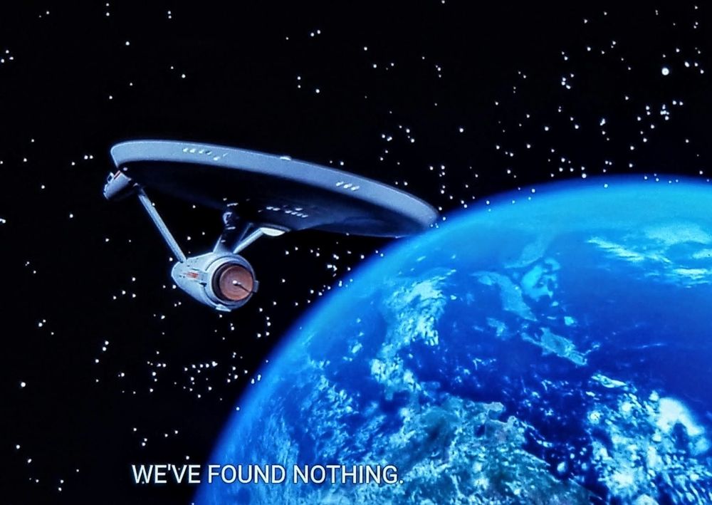 Star Trek The Original Series scene. scene is viewing an Earth like planet with stars in the background. The Enterprise is orbiting, closed caption reads, "We've found nothing."