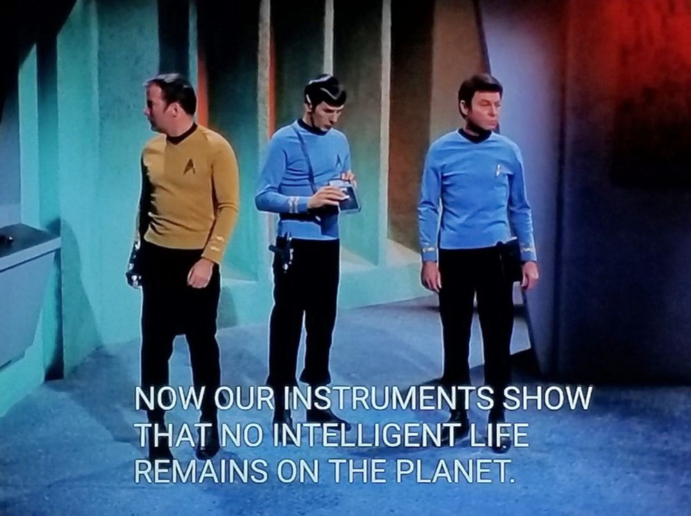 Star Trek The Original Series scene. Spock, Bones, and Kirk stand looking around in an off-ship room. There's a thing on the wall that kind of looks like one of those school water bubblers that shoots a little arc of water. Spock is reading his tricorder. Closed caption reads , "NOW OUR INSTRUMENTS SHOW THAT NO INTELLIGENT LIFE REMAINS ON THE PLANET"