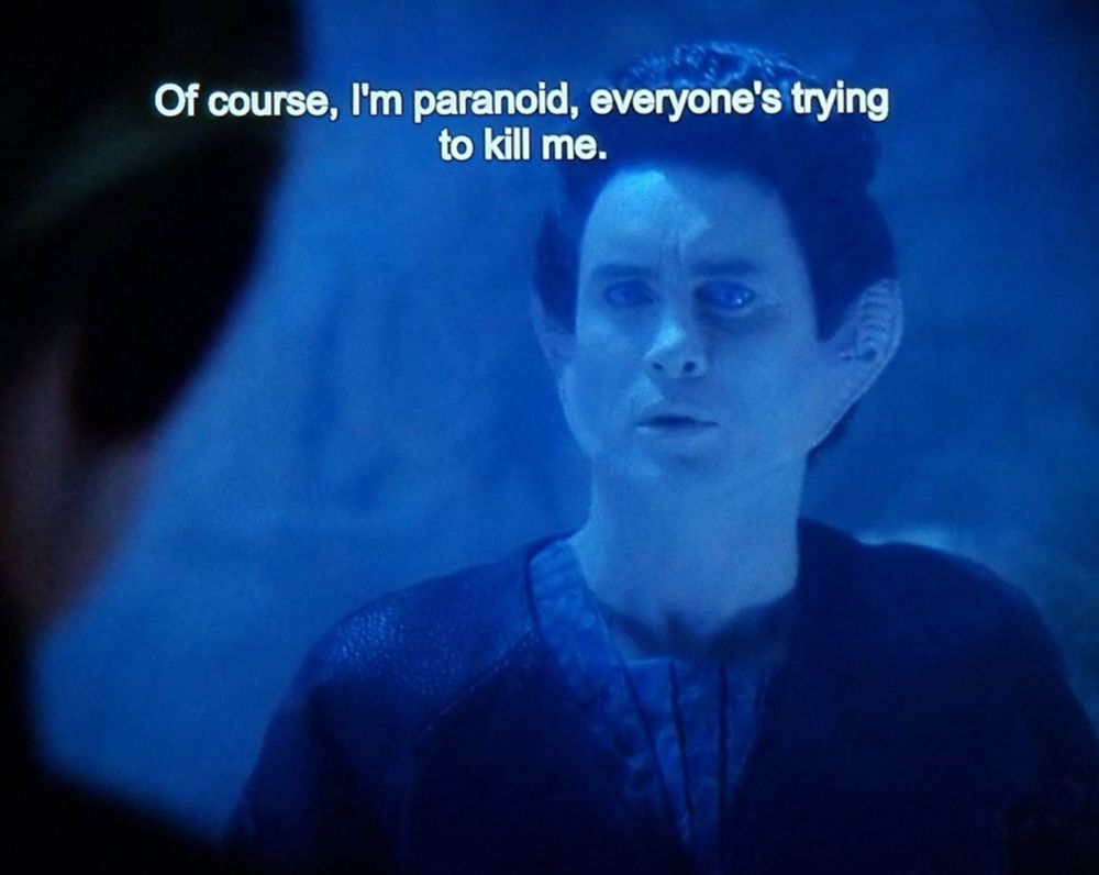 Deep Space Nine scene. Weyoun is pictured in a dark cave. Weyoun is an alien with human features aside from long but not wide ears that stretch further down the jawline and look ribbed. He's talking to someone and looks spooked. Closed caption reads, "Of course, I'm paranoid, everyone's trying to kill me."