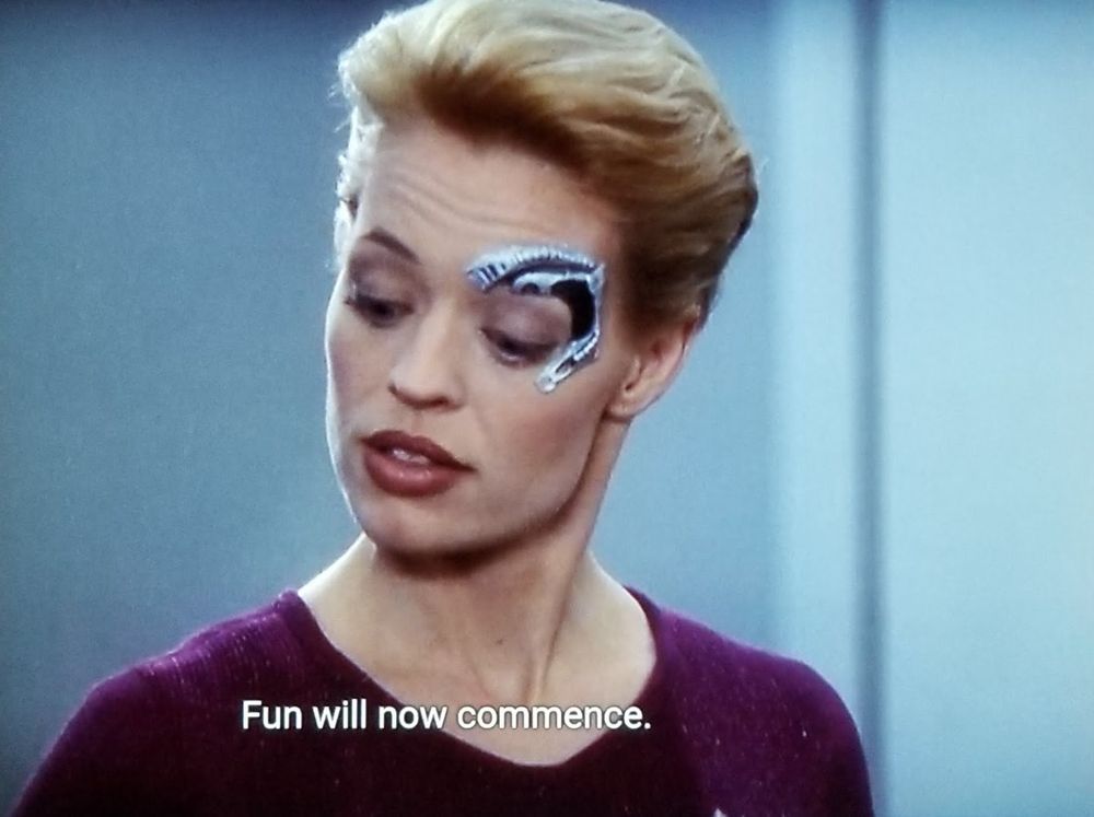 Star Trek Voyager scene. Seven of Nine (tertiary adjunct of unimatrix 01) is pictured. She has a dolphin shaped metal robotic implant around her left eye because she is a borgs. Closed caption reads, "Fun will now commence."