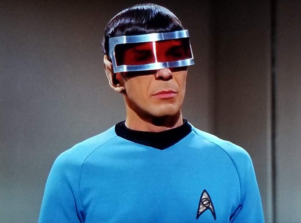 Star Trek The Original Series scene. Spock is pictured, in blue uniform, and he's STANDING. He's wearing a large red visor over his eyes. There's no cutout for the nose, so it's just a one long panel of red wrapping around the top of his face with silver framing. It looks like a chill AF pair of shades and *probably* serves an actual purpose, but we don't know, it's just a screenshot. No caption. 