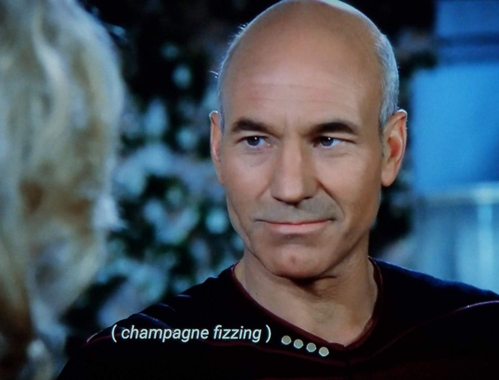 Star Trek The Next Generation scene. Early series Picard is shown up close with a determined look of contentment. He's locked into eye contact with someone just off screen, and smouldering. Closed caption reads: (champagne fizzing)