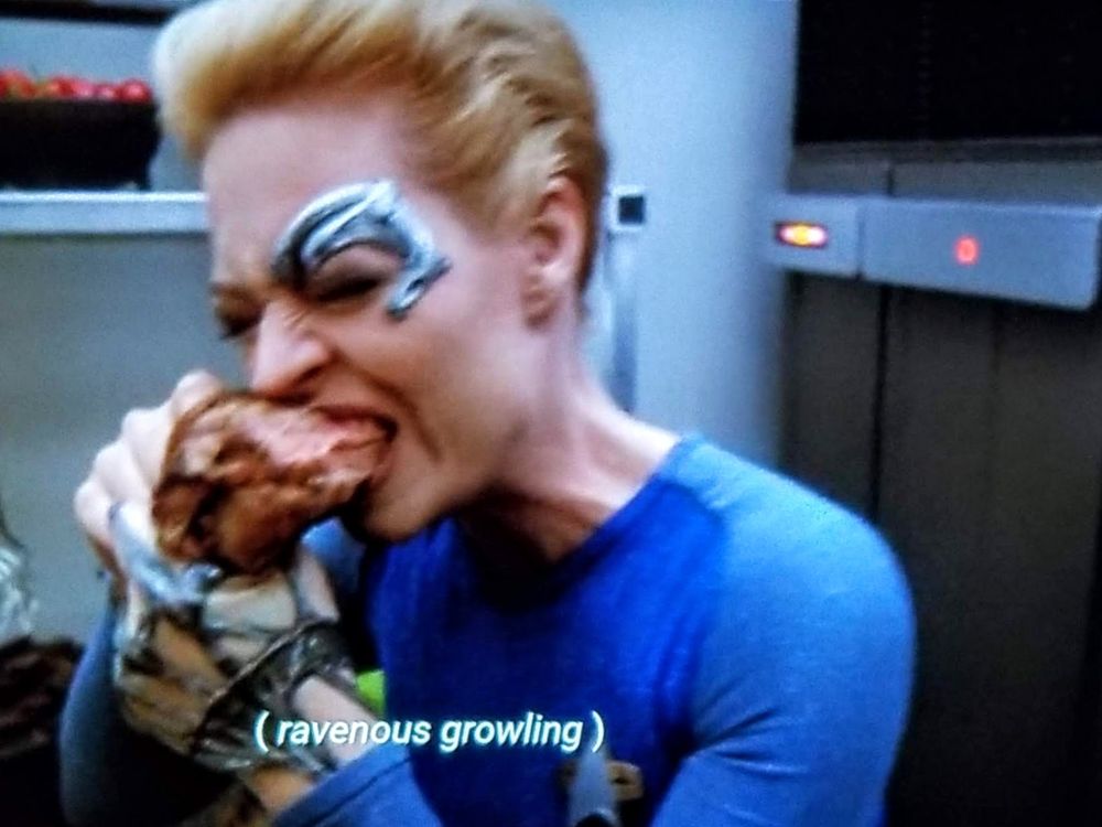 Voyager scene. Seven of Nine, Tertiary Adjunct adjunct of Unimatrix-01, is seen up close absolutely devouring a big ol' turkey leg like some kind of vicious animal. It's one of those tin foil wrapped Renaissance festival turkey legs, absolute unit. Closed caption reads: (ravenous growling)