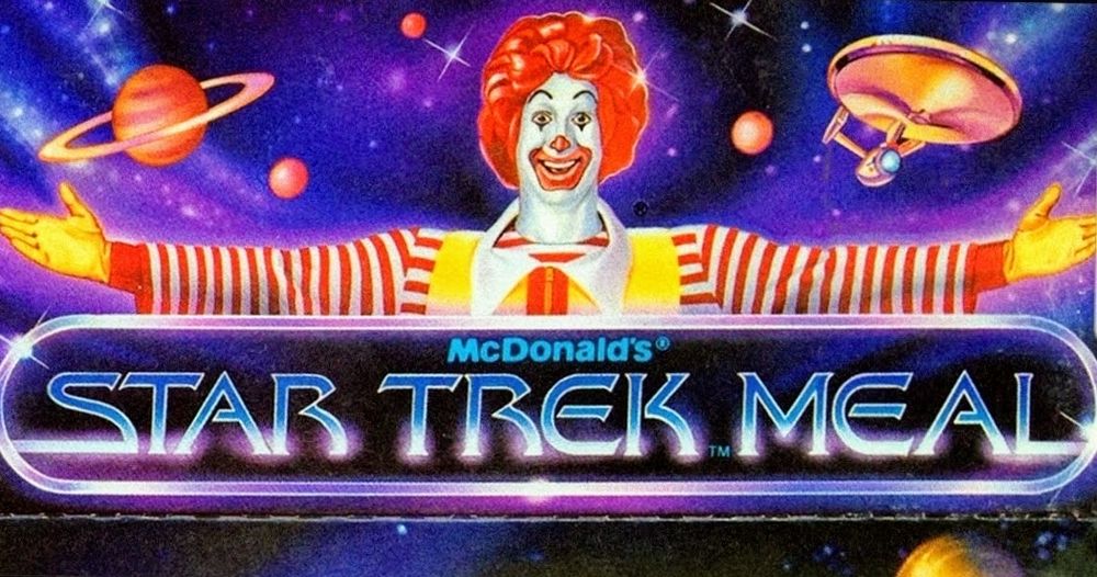 Advertisment (British pronunciation in my brain because it's better than how we say it in America) for a McDonald's happy meal. Ronald McDonald, famous clown, stands with arms wide open. Behind him is outer space with some planets and stars and nubulars with the Enterprise flying. But this picture is like cartoony not photoey. In front of Ronald the aforementioned clown is a sign that reads "McDonald's STAR TREK MEAL"