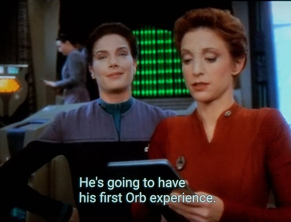 Star Trek Deep Space Nine scene. Kira and Dax are standing in the ops bullpen on station. Kira is reading off a PADD, with Dax just to her side and looking pretty far out daydreamy trippin balls about something. Closed caption reads, "He's going to have his first Orb Experience.