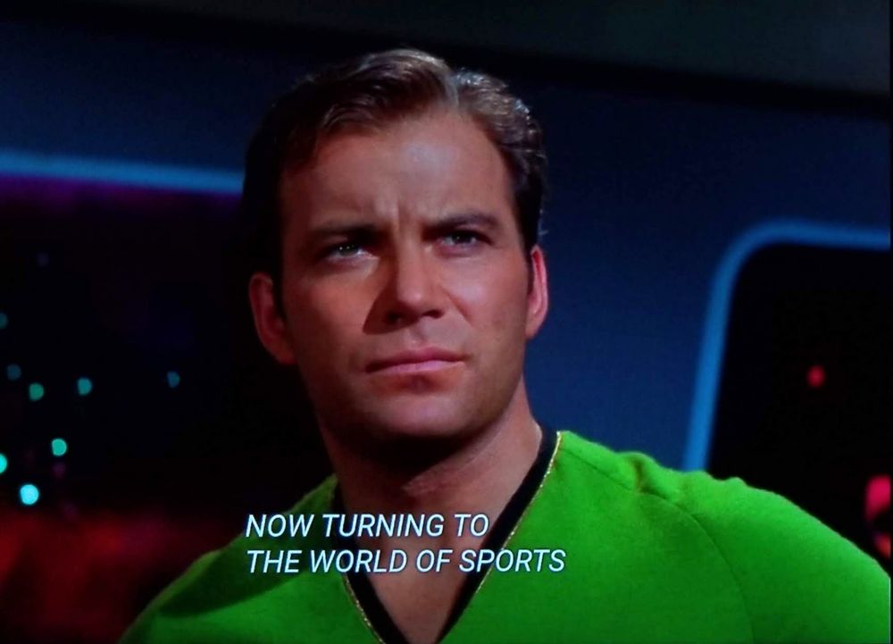 Star Trek The Original Series scene. We're close in on Kirk on the bridge in his ecto-cooler green uniform. He's standing and looking forward with slightly furrowed brow and concentration. Closed caption reads, "Now turning to the world of sports."