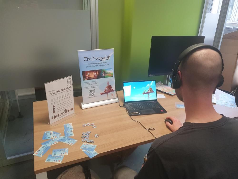 Back of someone's head wearing headphones and playing the game 'The Protagonish' on a laptop, and two banners, one for The Protagonish, and one for another forthcoming game...