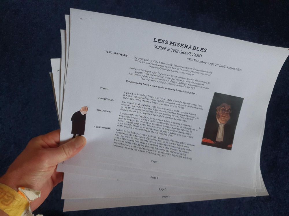 Hand holding printed scripts (lots of text and a couple of character images), 'Less Miserables' is visible at the top of the page
