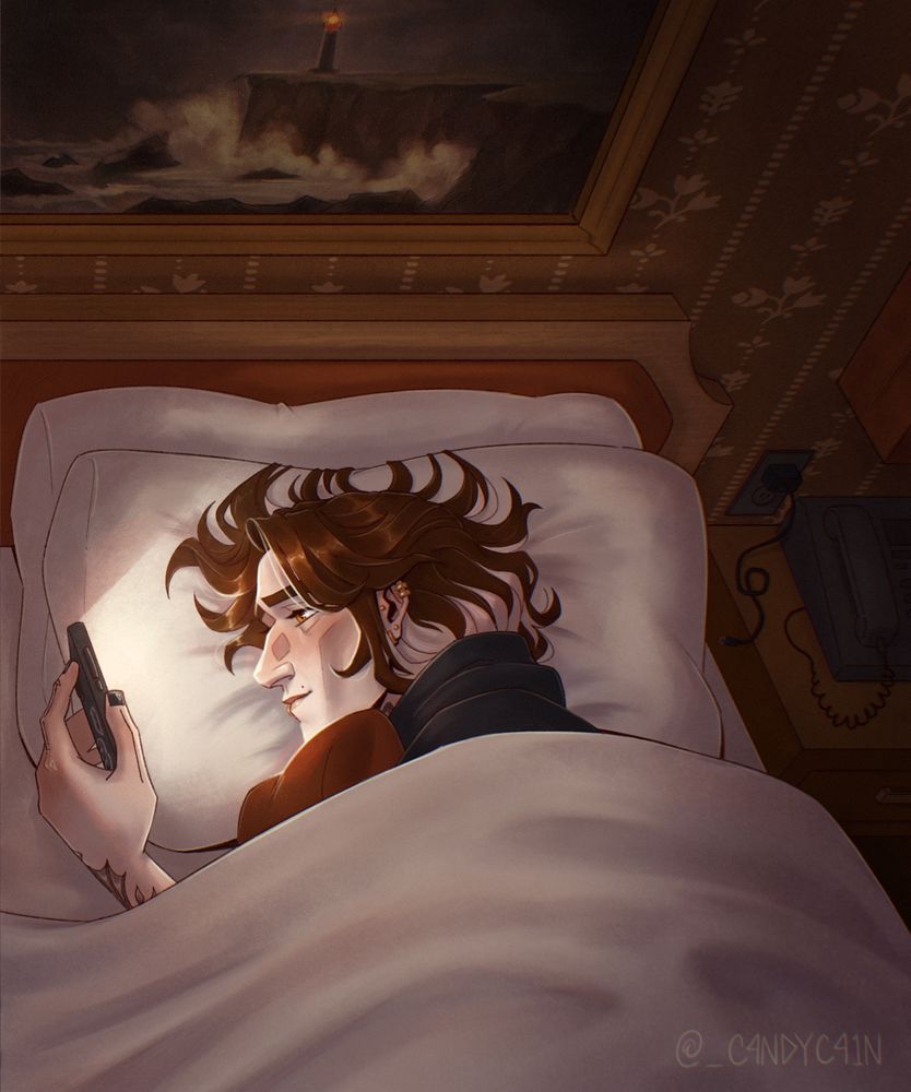 Viktor snuggled into a hotel bed video calling on his phone. A framed painting of a lighthouse in a storm hangs above the bed