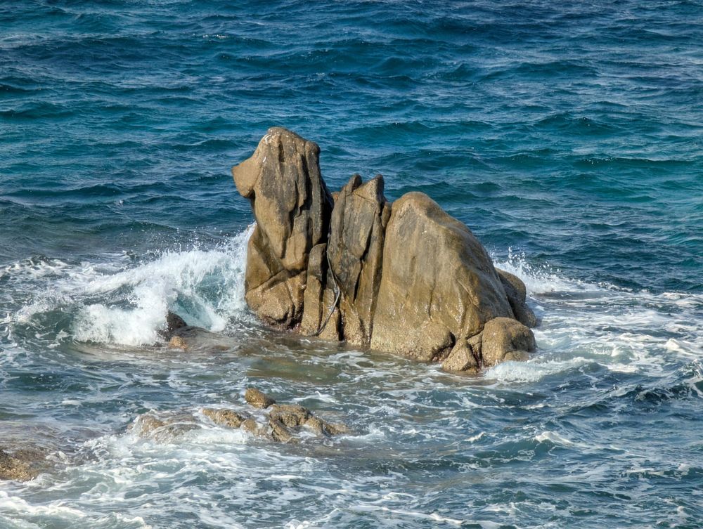 A rock shaped like a camel splashes in the surf near Little Venice, Mykonos