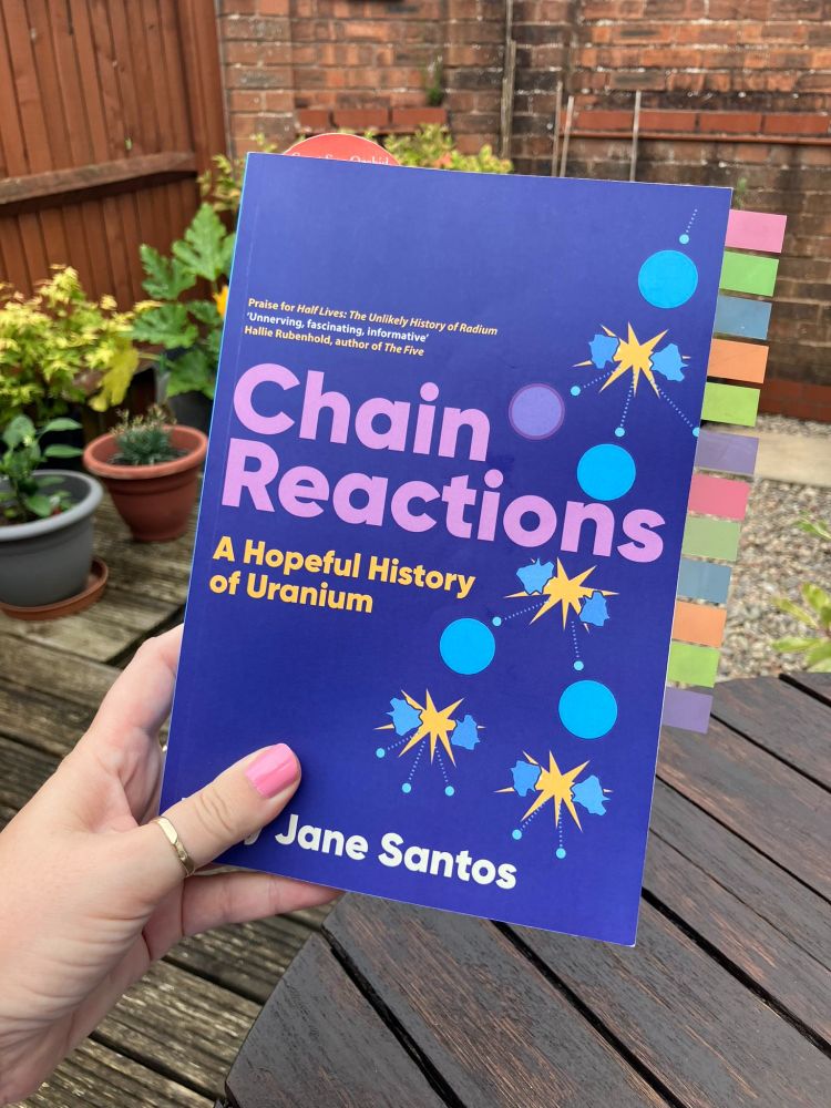 Hand holding a copy of Chain Reactions A Hopeful History of Uranium. The book has lots of colourful tabs showing wear the reader has marked sections.
