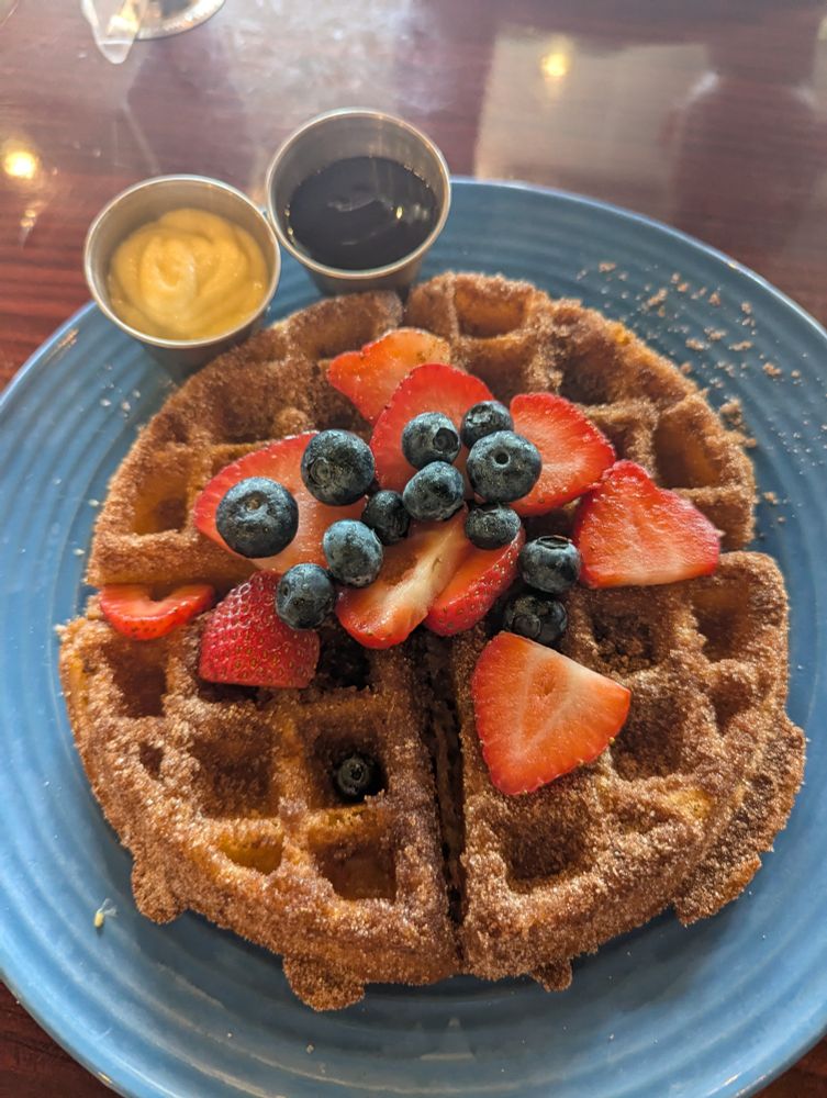 A fried cinnamon-sugar Belgian waffle with berries, chocolate sauce, and a cream sauce topping