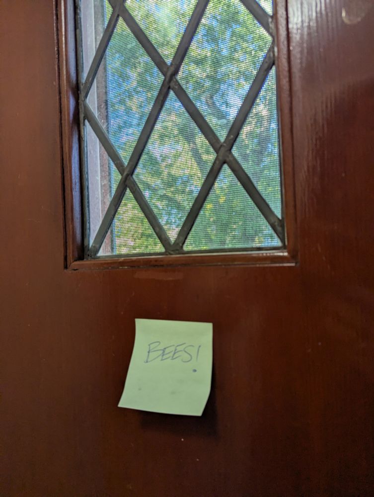Inside of a front door, with a single sticky note upon it, which reads, "BEES!" it would seem to imply there are bees, in large quantities, just outside of this door