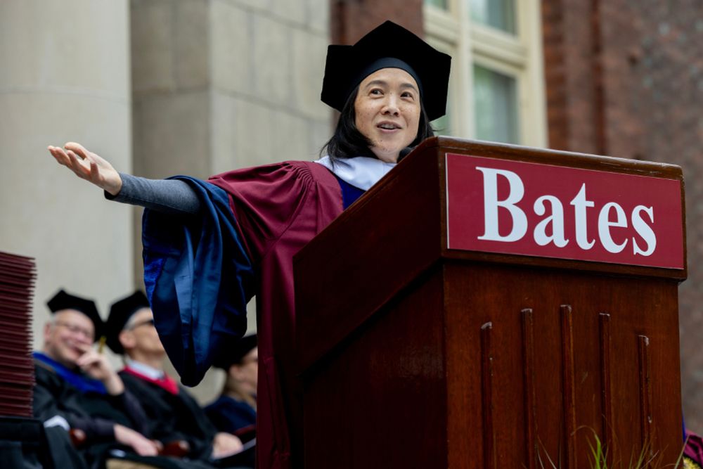 Angela Duckworth gestures to her right (our left) behind a podium with the Bates wordmark during the 2025 Bates Commencement address on Sunday, May 25, 2025.
