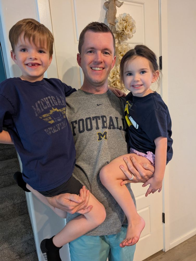 My annual picture holding my two kids, all of us in Michigan shirts. I am not yet struggling to pick them both up 