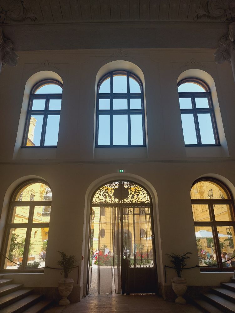 Blick aus dem Durchhaus von Schloss Eckartsau (AT) in den sonnigen Innenhof ; 6 Fenster (davon eine Glastür) öffnen das Stiegenhaus zum Innenhof hin