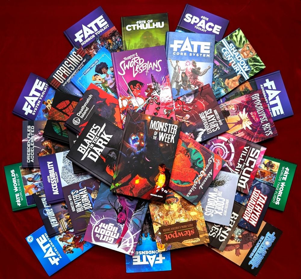 A literal pile of some of the RPGs we've published including Fate, Stewpot, Girl By Moonlight, Thirsty Sword Lesbians, Blades in the Dark, Deathmatch Island, and Monster of the Week.