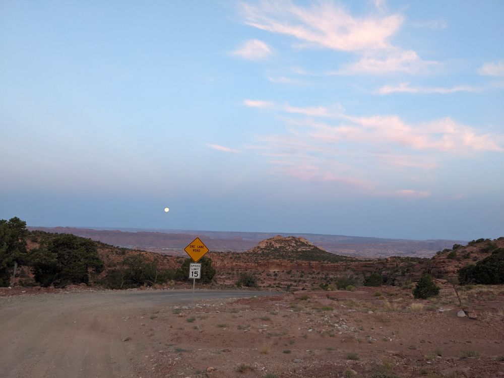 Over exposed image of a full moon setting over a desert landscape illuminated by twilight. 