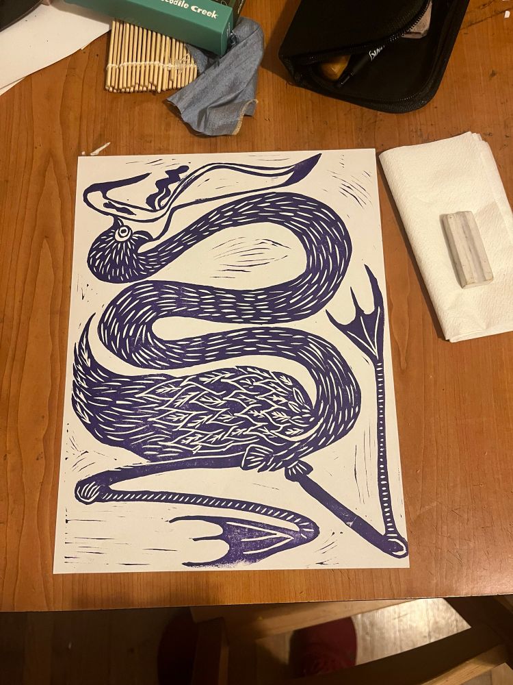 A block print of a freaky flamingo with a snakey neck. It’s yelling and its tongue is sticking out. This is a test print, purple on white paper. 