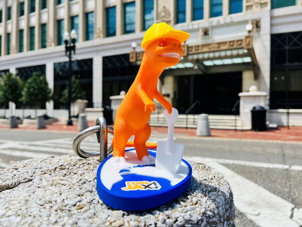 a plastic orange dinosaur with a yellow hard hat holding a white shovel