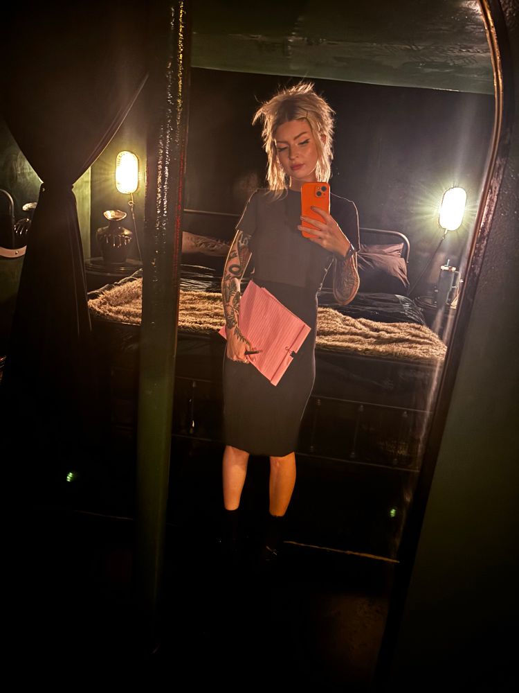 Goddess Hunter stands in front of a mirror with a pink notepad and pen. 