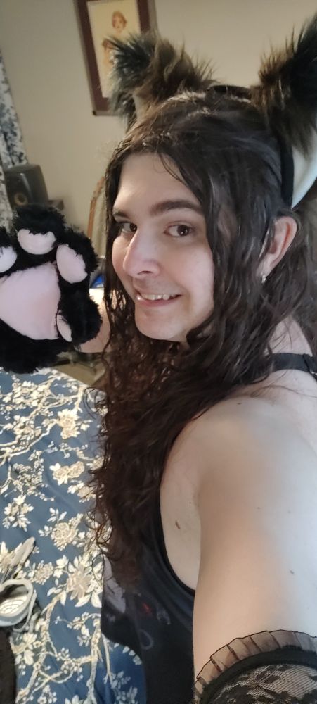 a girl in a black dress wearing cat ears and big bappy paws smiles at the camera