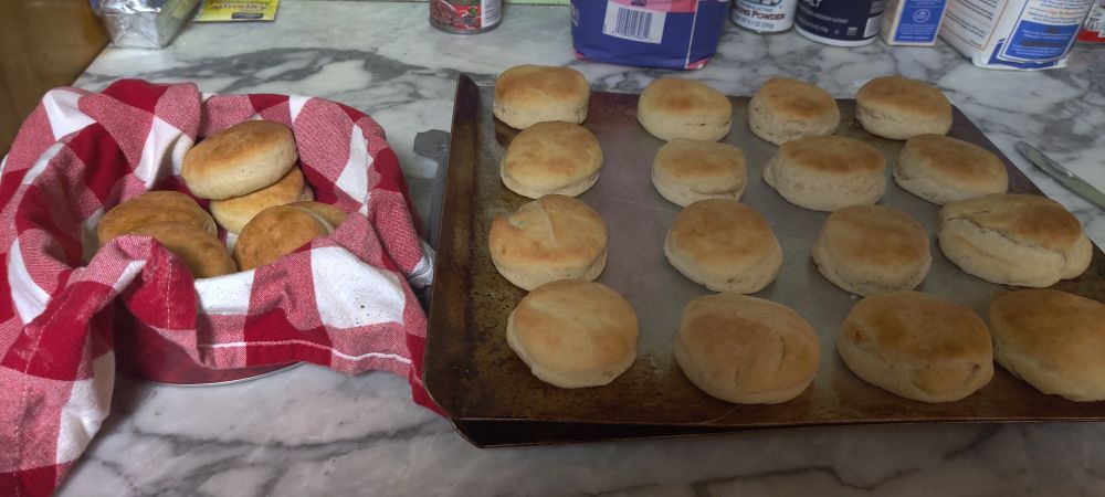 a decorative basket sits next to a baking tray. each holds a number of hot biscuits
