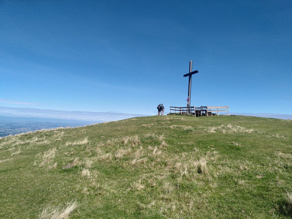 Un sommet herbeux avec une croix et deux randonneurs. 