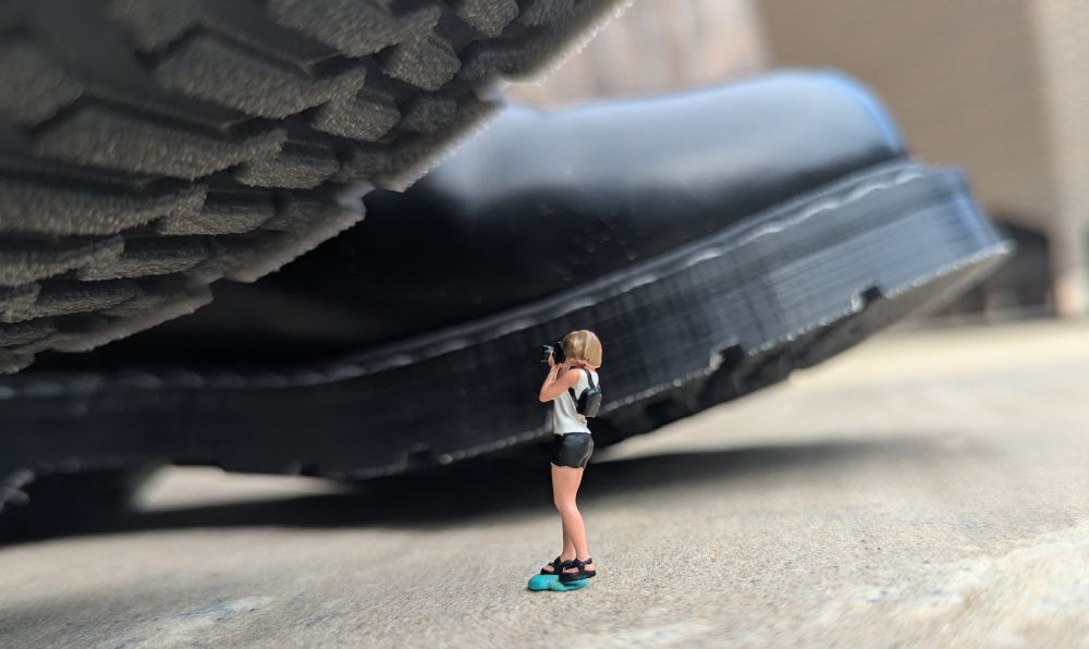 A figurine of a tiny woman photographer snaps a picture of my boot soles.