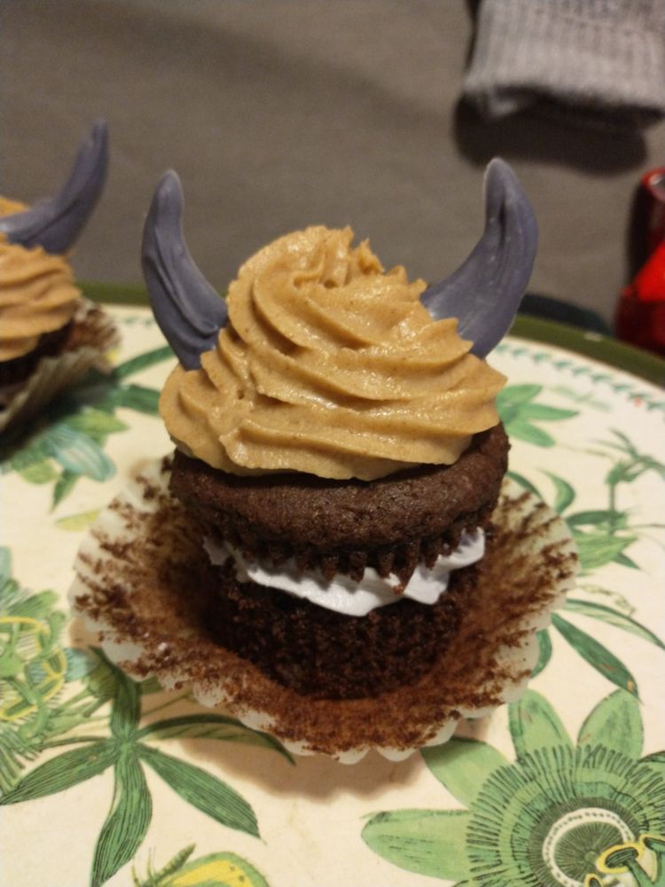 A photo of a cupcake, resembling the monster cake from the game Breath of the Wild. A chocolate sponge filled with light purple frosting, covered in light brown caramel frosting and two purple horns.