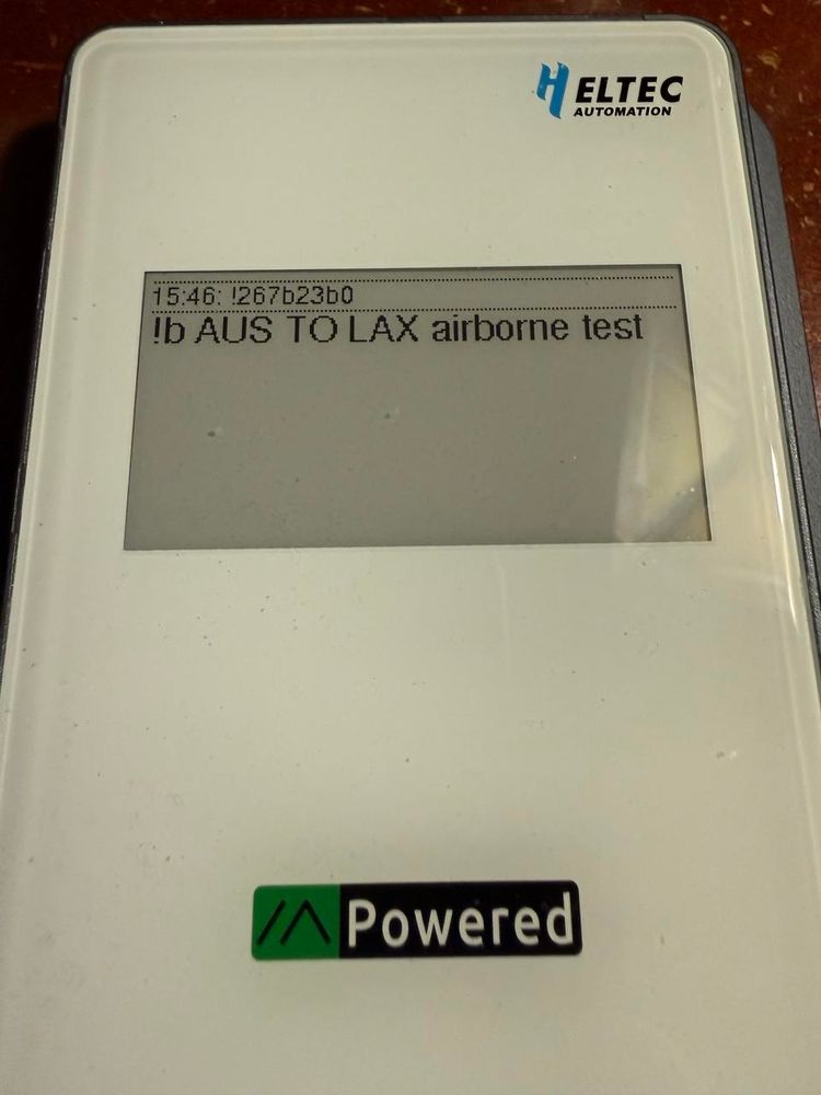 A Meshtastic device. The eink screen says !b AUS to LAX airborne test