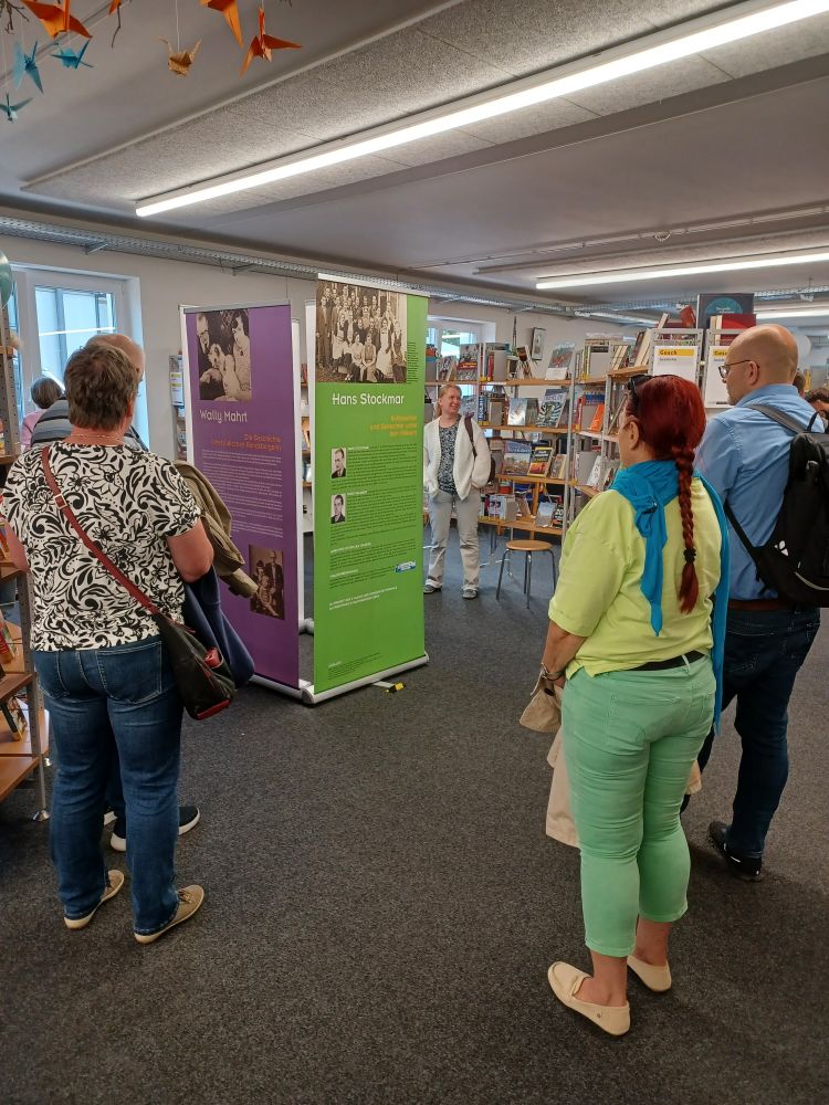 Besucherinnen und Besucher flanieren durch die Stadtbücherei Kaltenkirchen zu den verschiedenen Exponaten der Ausstellung. Hier vor dem neuen Beitrag zu Hans Stockmar, einem Gerechten unter den Völkern.