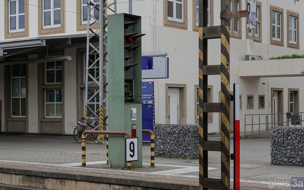 H/V Hauptsignal am Bahnsteig in grüner Einhausung, sodass aus der seitlichen Perspektive nur ein Teil des Schirms sichtbar ist.