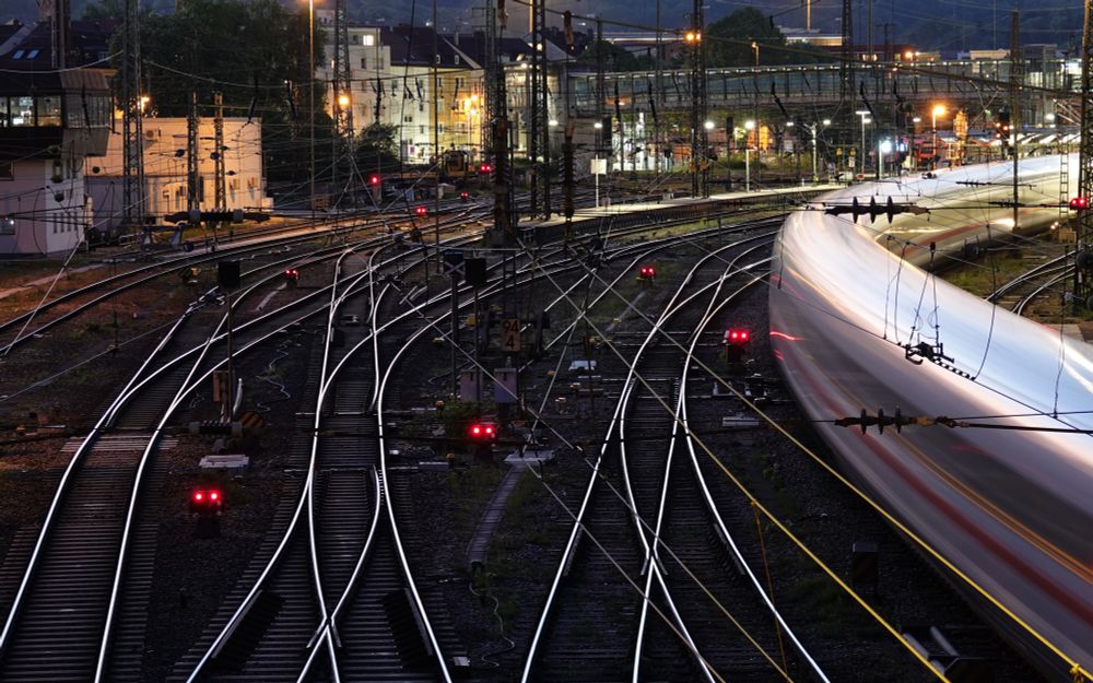Es ist abends und dunkel: Blick auf ein Gleisfeld von einer Brücke, wobei die Schienen hell zu leuchten scheinen