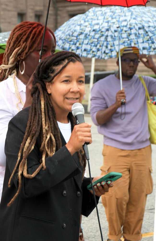 Robyn speaks in a black Balzer with her hair down to her shoulders holding a mic