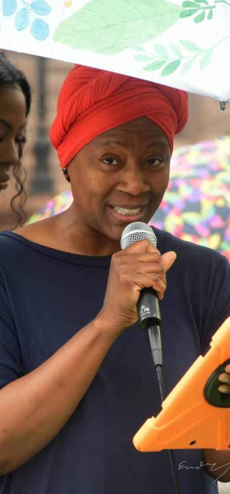 A speak in a red headscarf holds a mic and speaks loudly
