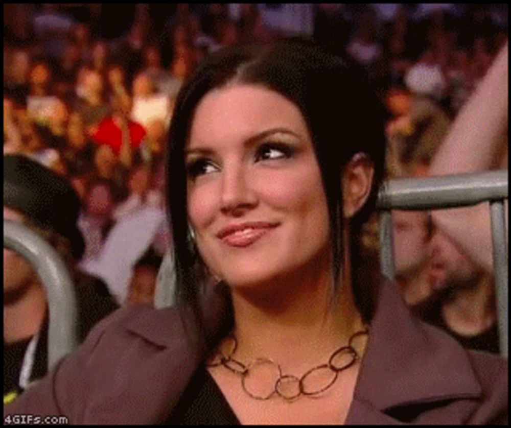 a woman wearing a necklace is sitting in front of a crowd and smiling