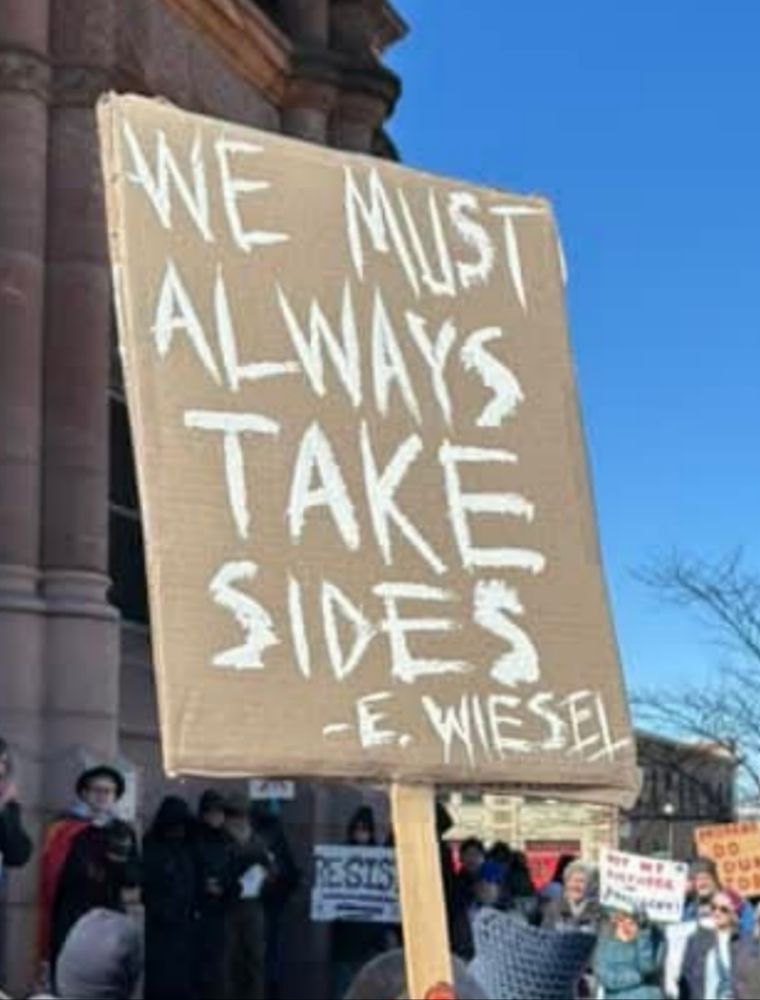 White paint on brown cardboard sign. Reads, "We must always take sides." -E. Wiesel.