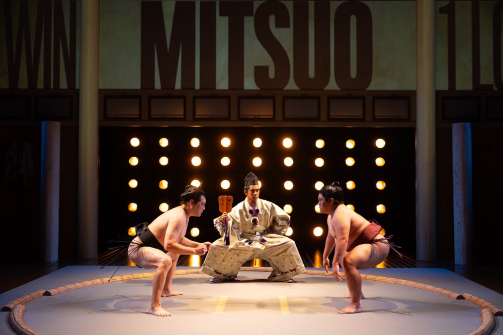 Two Japanese sumo wrestlers face each other in the dohyo, with a Gyoji (referee) between them. They are about to fight.