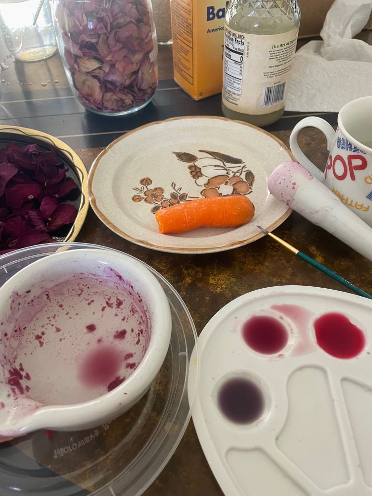 A white mortar and pestle sits next to a paint palette with watercolor made from dried rose petals 