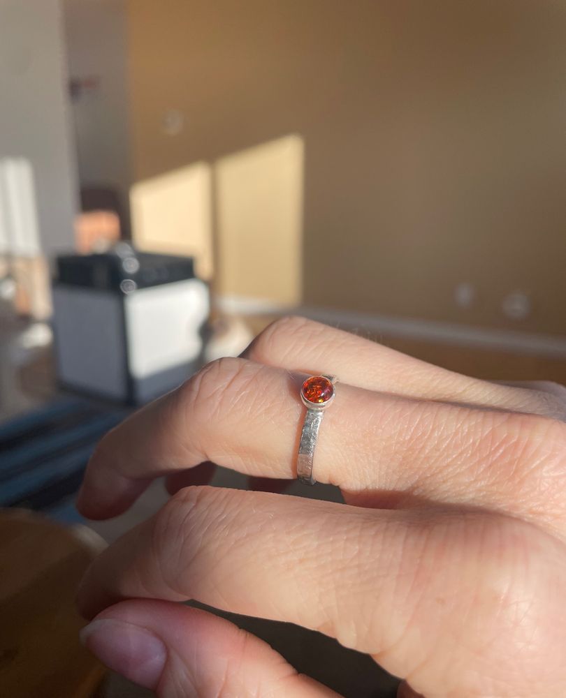 There is a simple silver ring set with a round piece of polished amber on the middle finger of Olives’ hand 